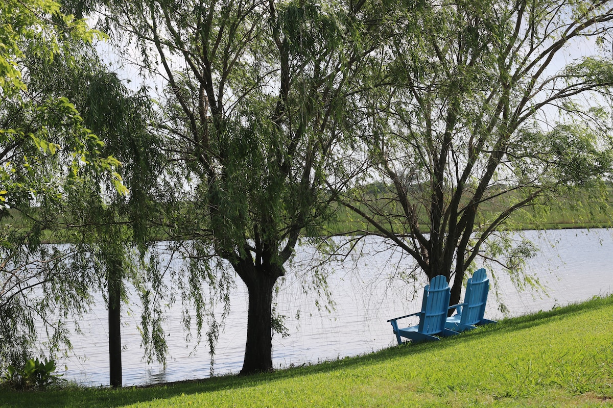 Willow trees and Adirondack chairs beside the pond
